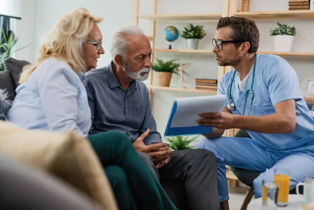Nurse navigator in blue scrubs explaining a mesothelioma treatment roadmap to a senior veteran and his daughter.
