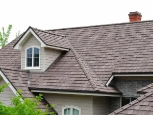 A close-up view of dark brown roof shingles and tan siding on an older home with a brick chimney, highlighting areas where asbestos-reinforced materials were commonly used